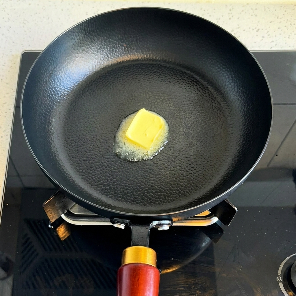 Un pezzetto di burro giallo che si scioglie in una padella nera calda.