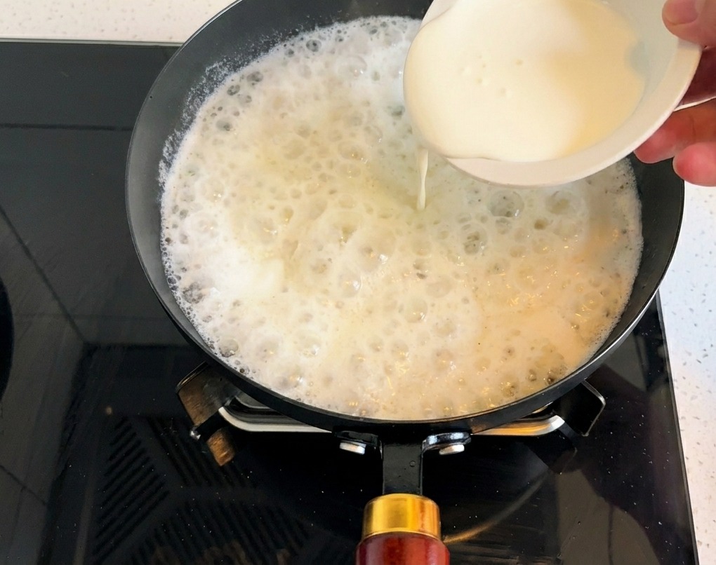 Panna liquida versata da una ciotolina nella base della zuppa che sobbolle.