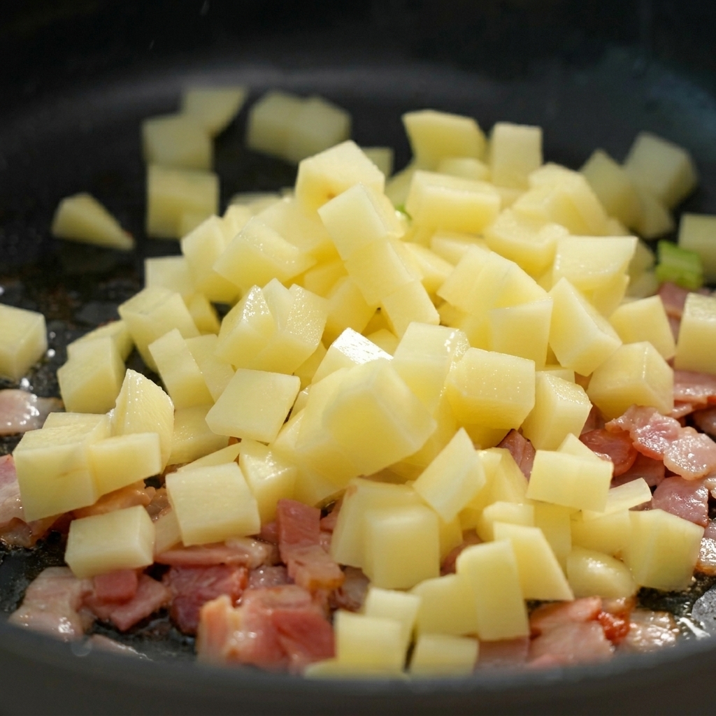 Cubetti di patate aggiunti nella padella insieme alla pancetta croccante.