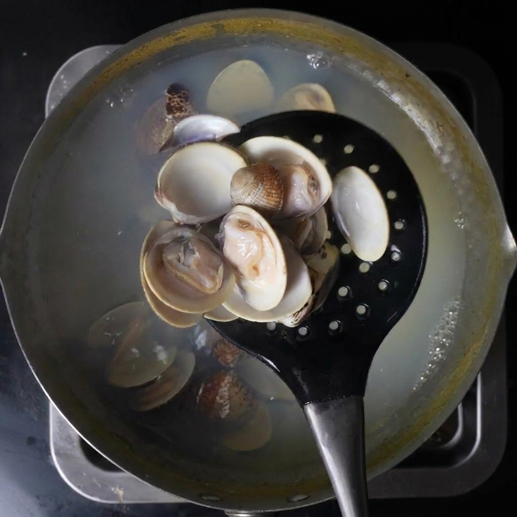 Un mestolo forato nero che solleva vongole aperte da una pentola di acqua bollente.