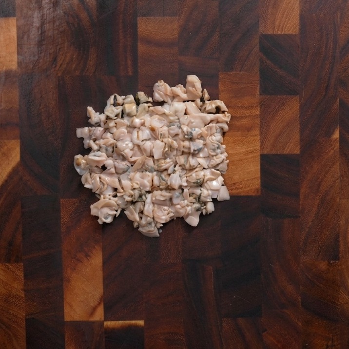 Un mucchietto di polpa di vongole tritata grossolanamente su un tagliere di legno scuro.