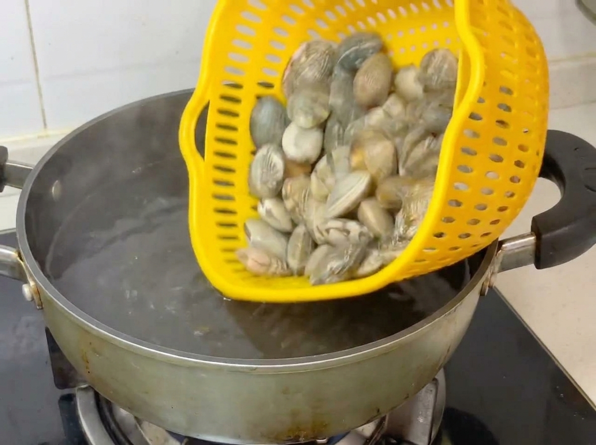 Vongole intere versate da un colino giallo in una pentola dacqua bollente.