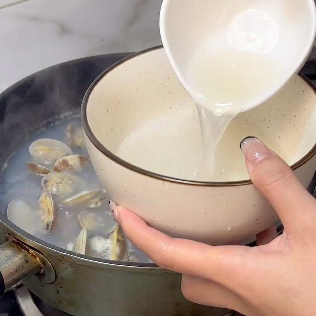 Una mano che raccoglie il brodo fumante con una ciotolina bianca da una padella.