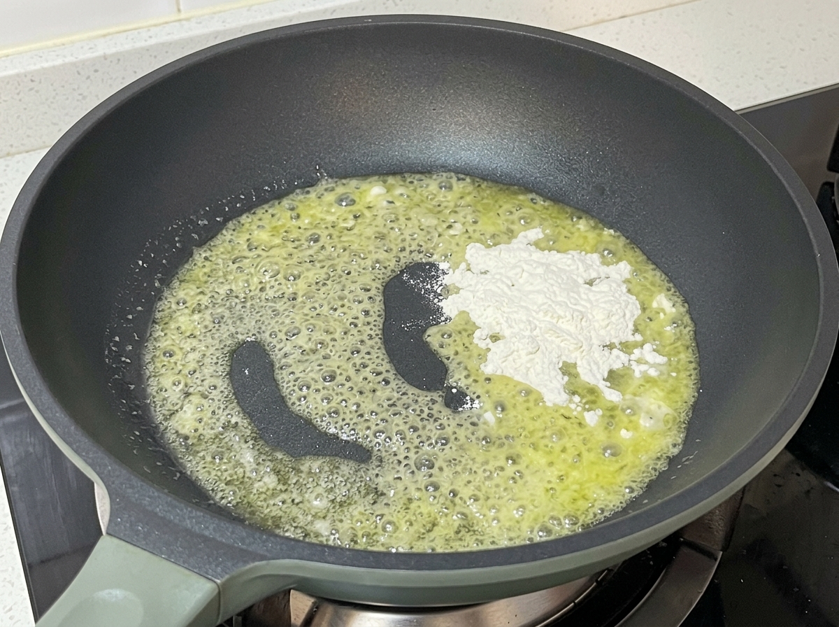 Padella sul fuoco con burro fuso spumeggiante e una manciata di farina bianca che viene mescolata.