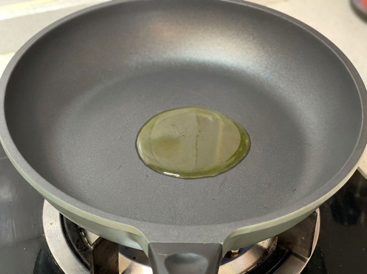 Un piccolo cerchio di olio doliva dorato al centro di una padella grigio scuro su un fornello a gas.
