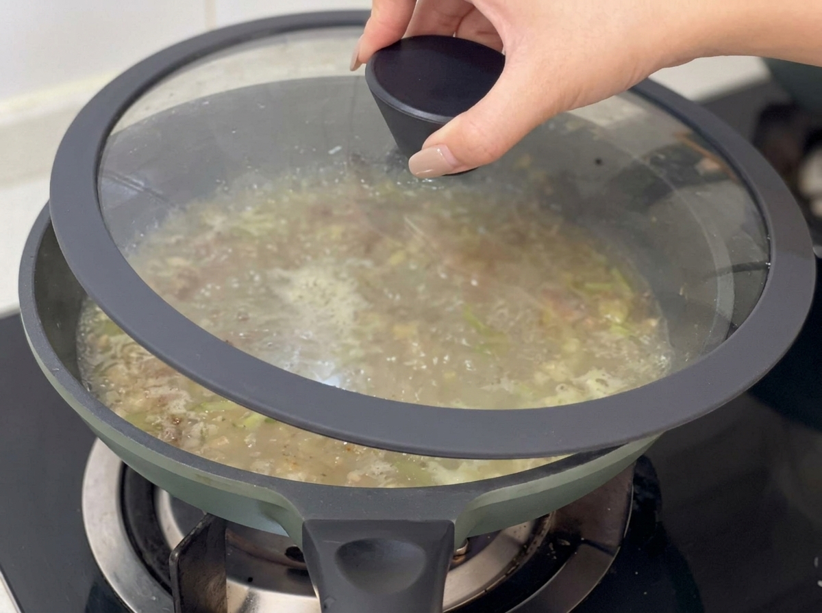 Mano che posiziona un coperchio di vetro sopra la padella con la zuppa che sobbolle.