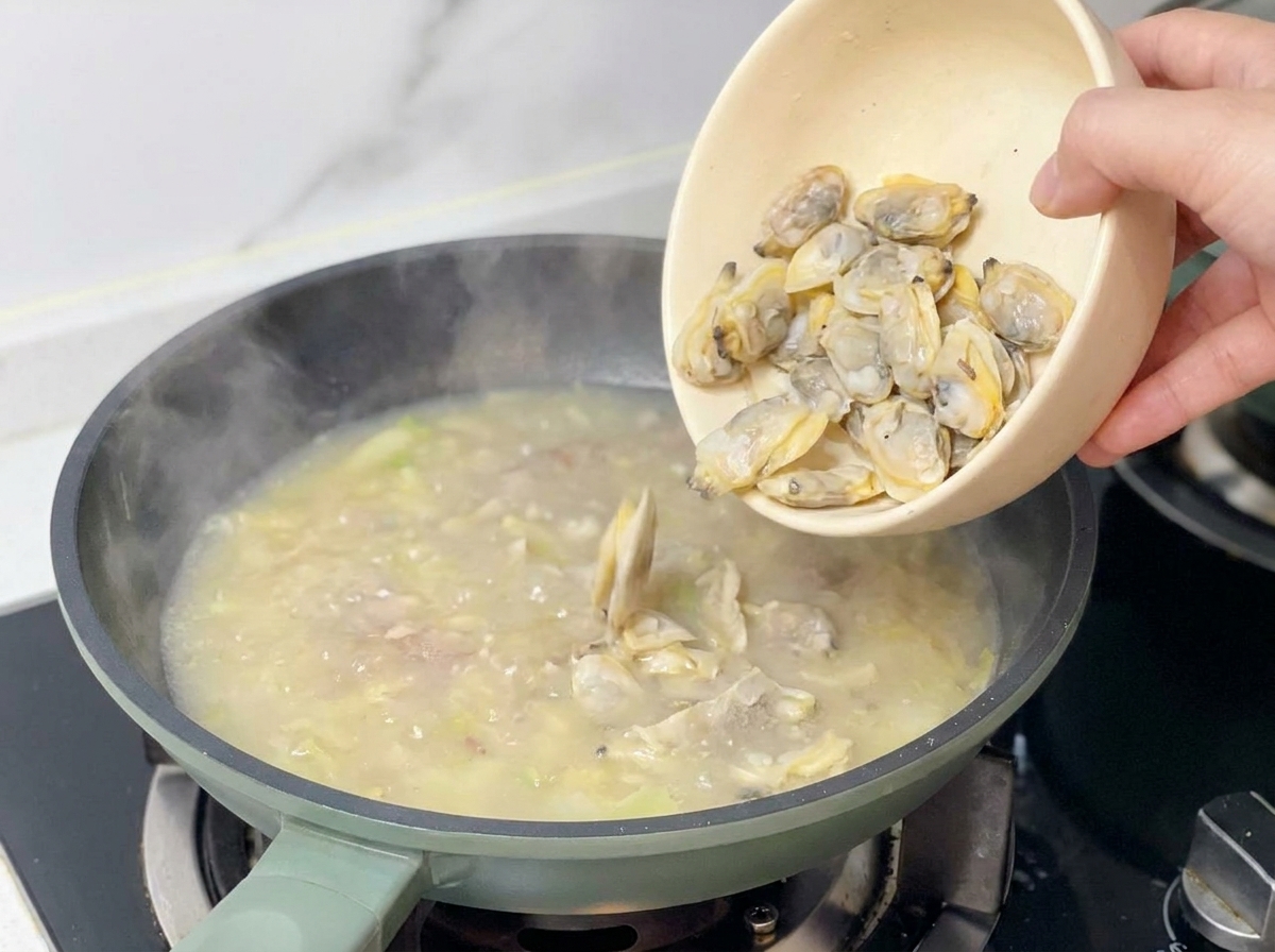 Mano che versa i molluschi di vongola cotti da una ciotola beige nella padella della zuppa.