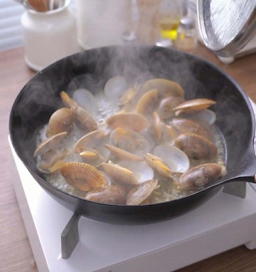 Vapore che fuoriesce da una padella di vongole cotte con i gusci bene aperti.