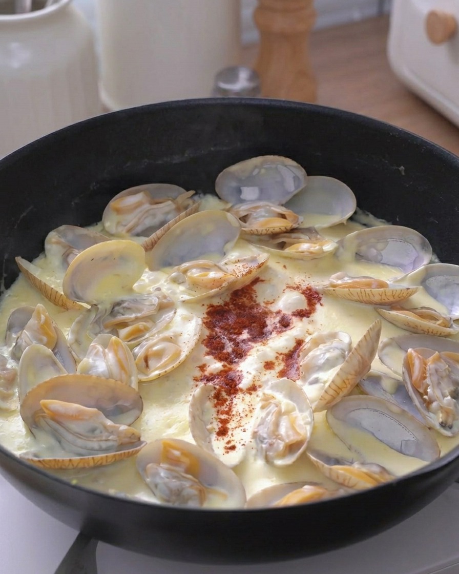Un pizzico di spezia rossa spolverata su una padella di vongole alla crema.