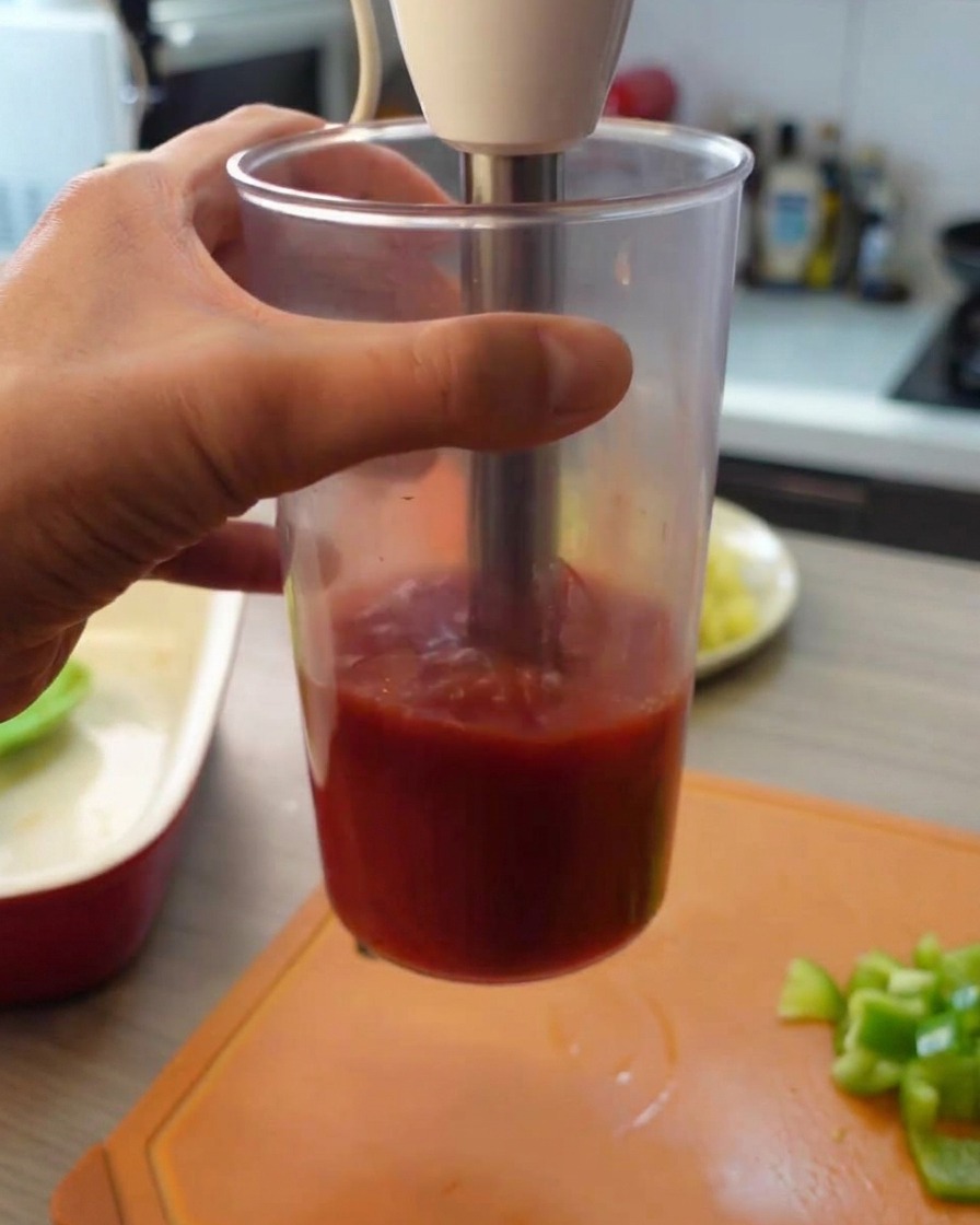 Uso di un frullatore a immersione per ridurre in purea i pomodori allinterno di un alto bicchiere trasparente.