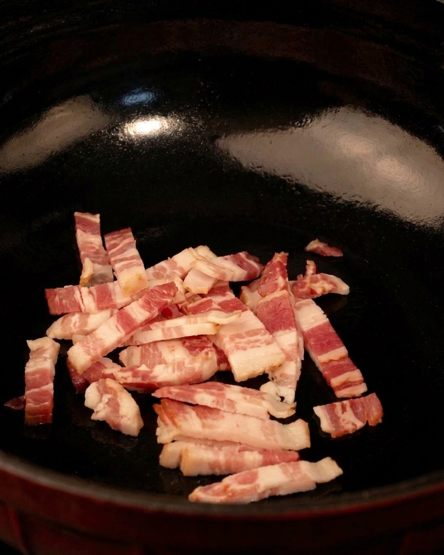 Cubetti di pancetta cruda in una padella nera, pronti per essere cucinati a fuoco medio.