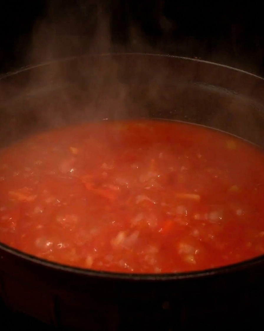 Una pentola fumante sul fuoco con zuppa di vongole rossa al pomodoro che sobbolle.