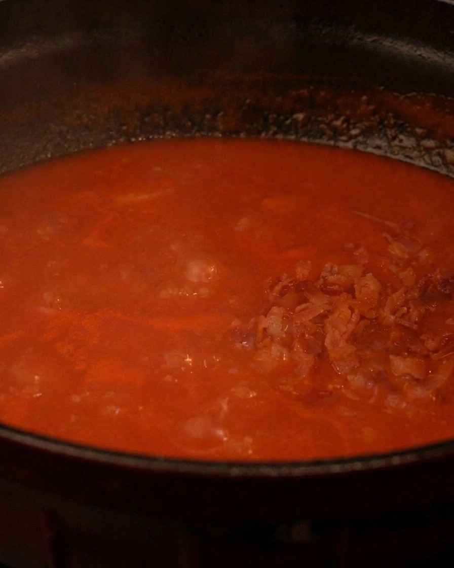 Pezzetti di pancetta croccante aggiunti a una pentola di ricca zuppa di pomodoro che bolle.