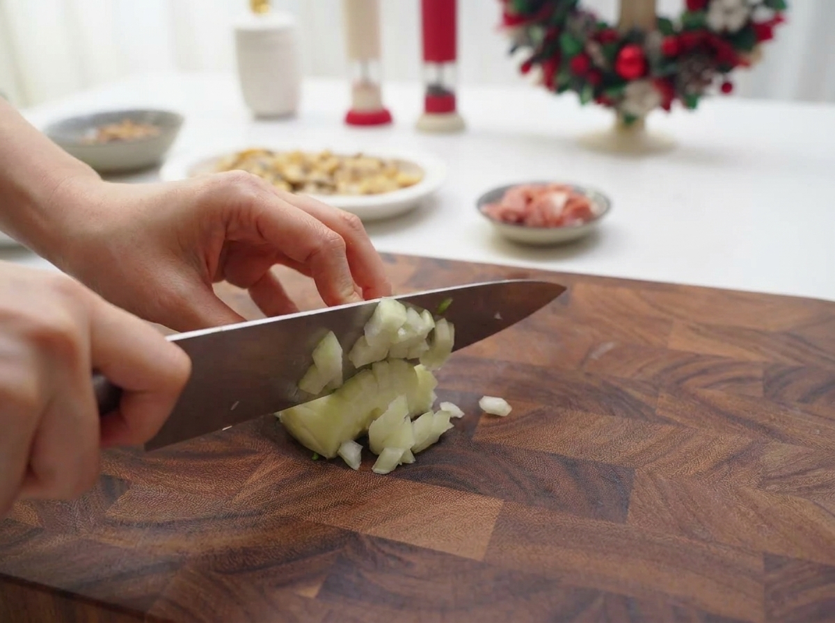 Mani che usano un coltello da chef per tritare finemente una cipolla bianca su un tagliere di legno.