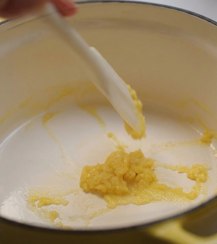 Una spatola di silicone bianco che mescola una pasta densa di burro e farina in una pentola gialla.