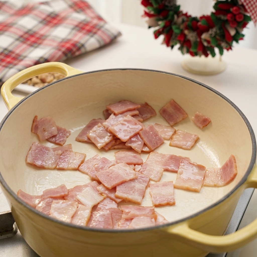 Quadretti di pancetta che friggono rilasciando il grasso in una pentola smaltata giallo pallido.