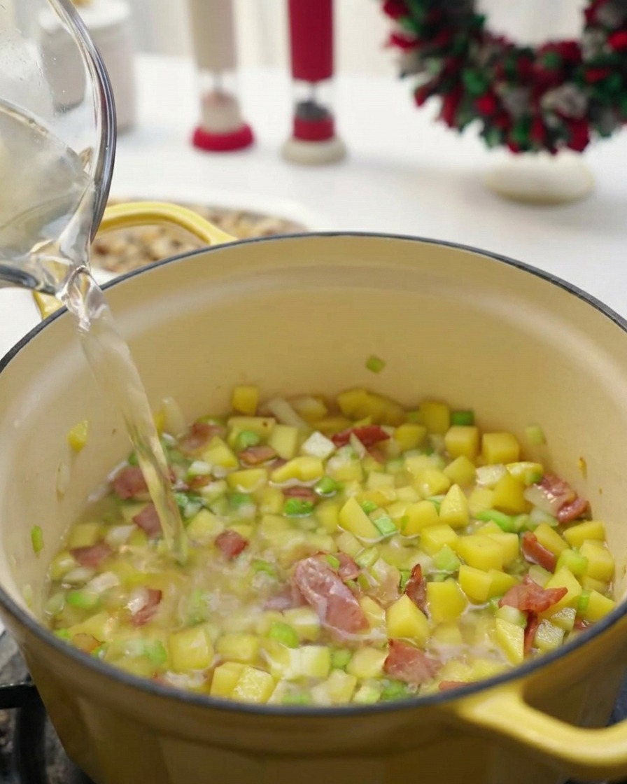 Liquido trasparente versato da una caraffa di vetro in una pentola gialla contenente verdure e pancetta.