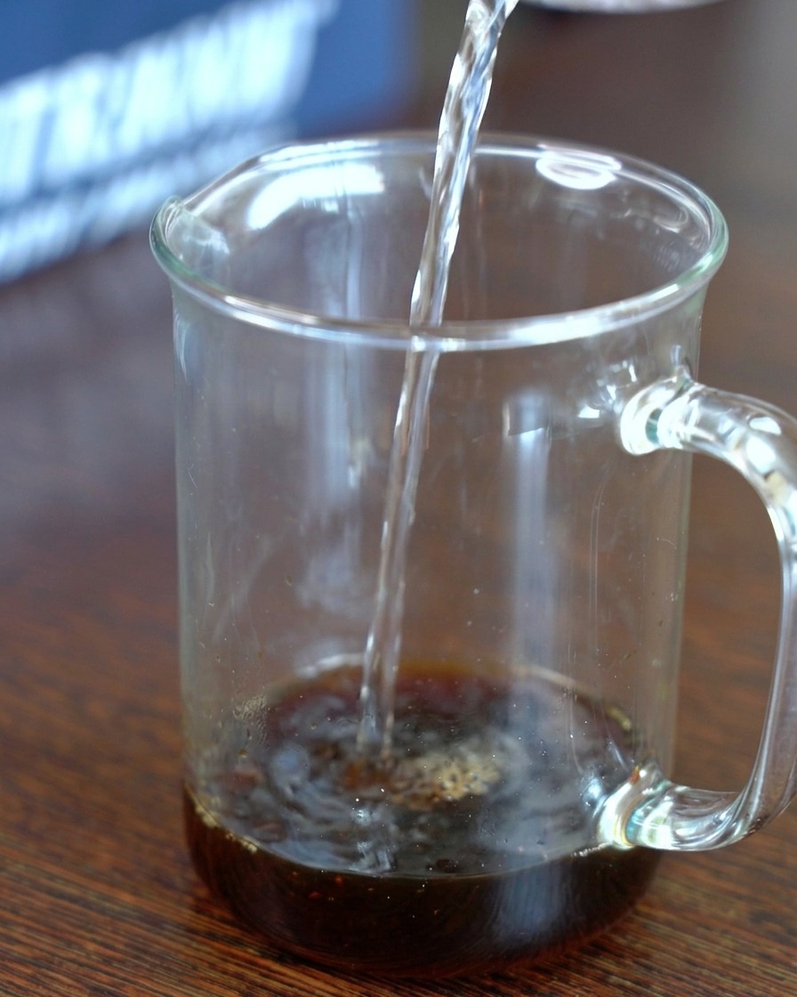 Acqua versata in un misurino di vetro contenente salsa di soia al kombu e zucchero.