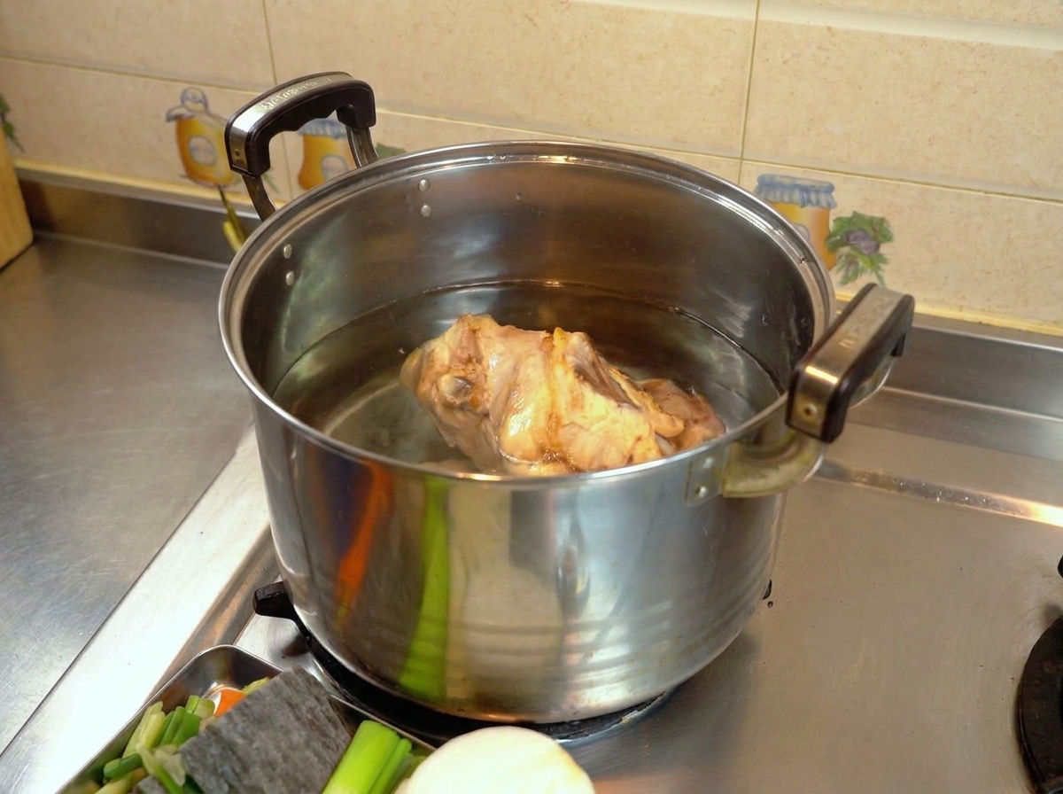 Una carcassa di pollo sbollentata in una grande pentola di metallo piena dacqua sul fornello.