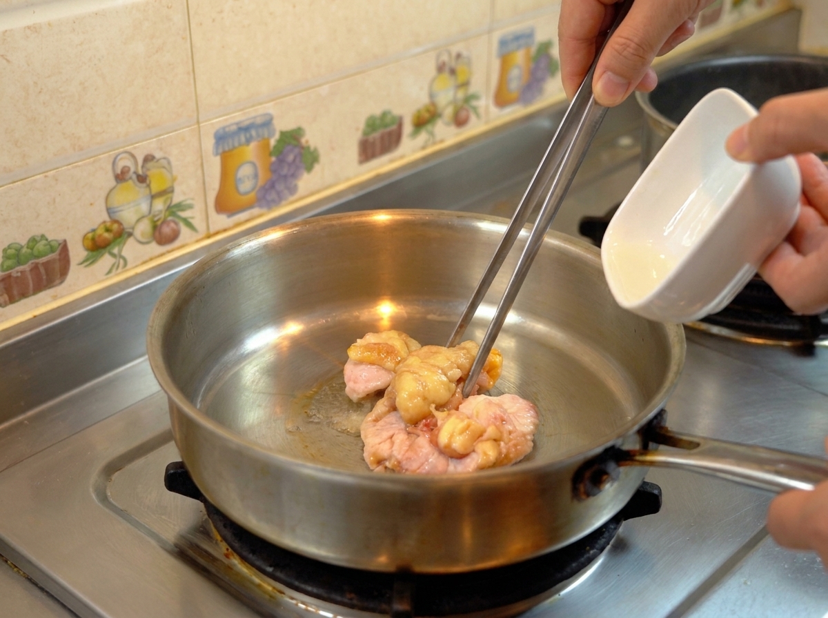 Pezzi di grasso di pollo crudo in una padella dacciaio mentre si sciolgono in olio limpido.