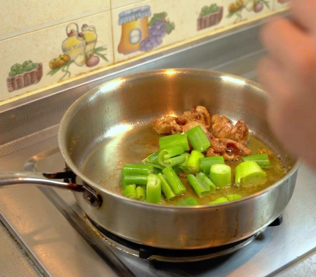 Foglie verdi di porro tagliate grossolanamente che friggono nel grasso di pollo dorato.