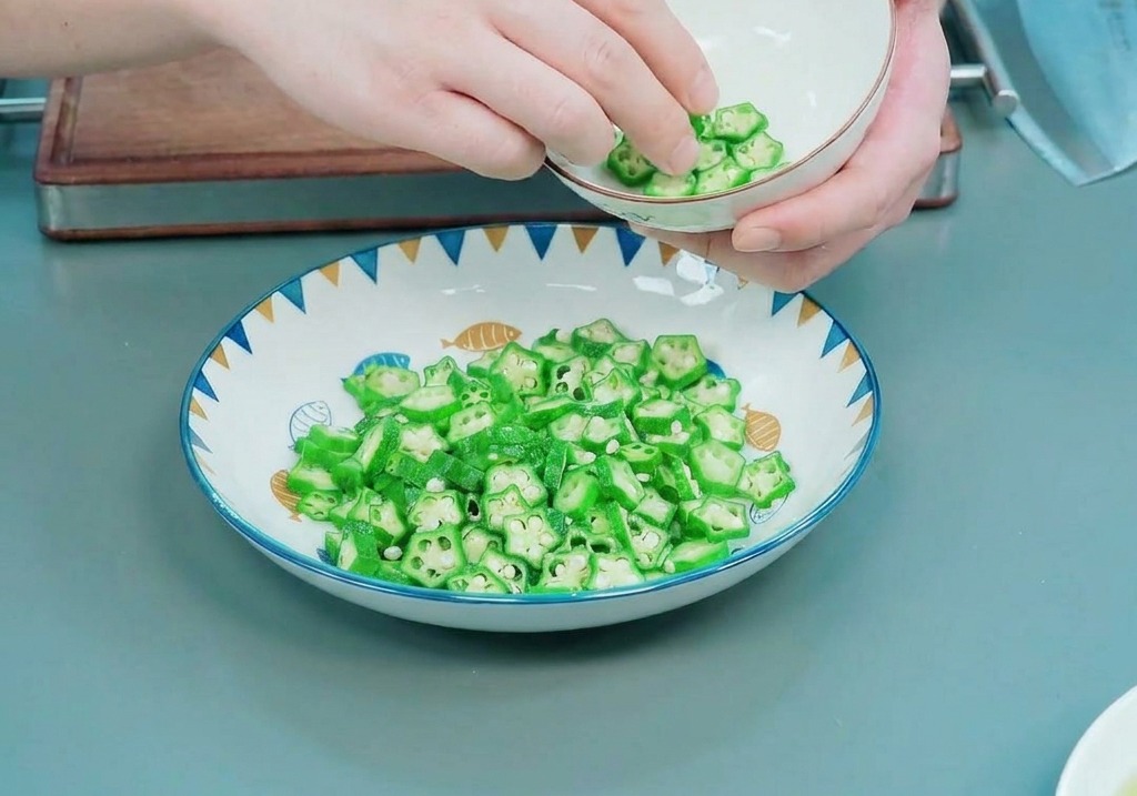Mani che rivestono con cura linterno di una ciotolina bianca con fette di okra a forma di stella.