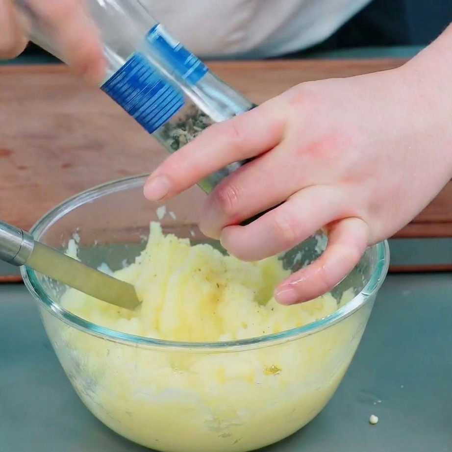 Mani che usano un macinapepe per aggiungere pepe nero e sale al purè di patate in una ciotola.