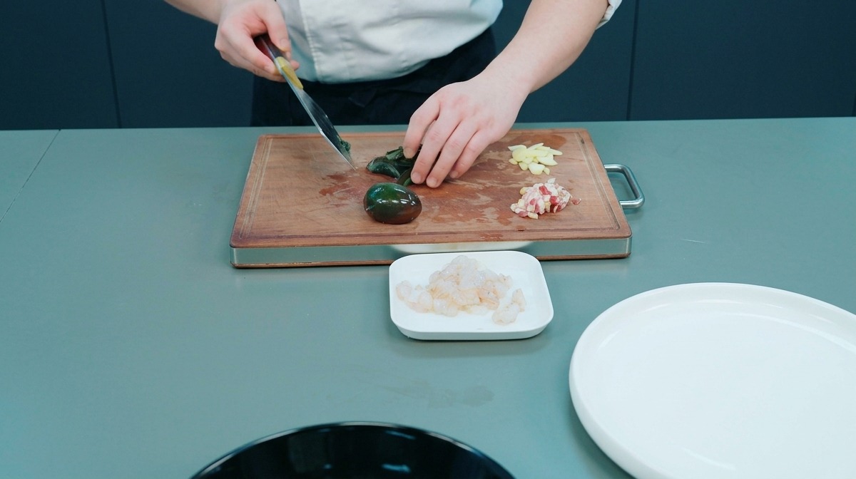 Chef che affetta un uovo dei centanni scuro su un tagliere insieme ad aglio e carne tritata.