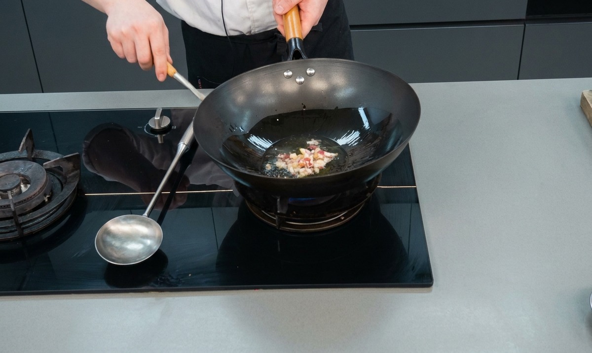 Carne tritata e aglio che sfrigolano in olio caldo allinterno di un wok nero.