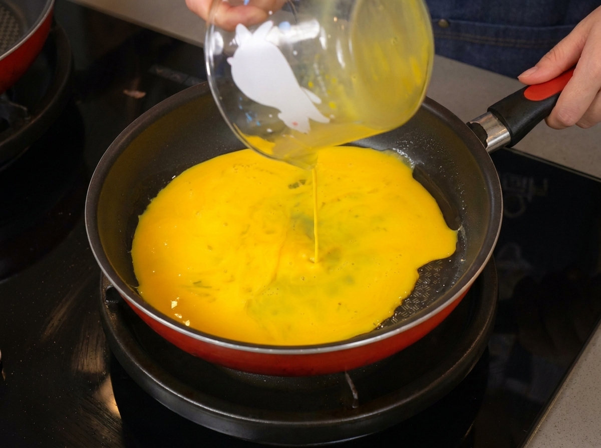 Uova sbattute di un giallo brillante versate da un misurino di vetro in una padella calda.