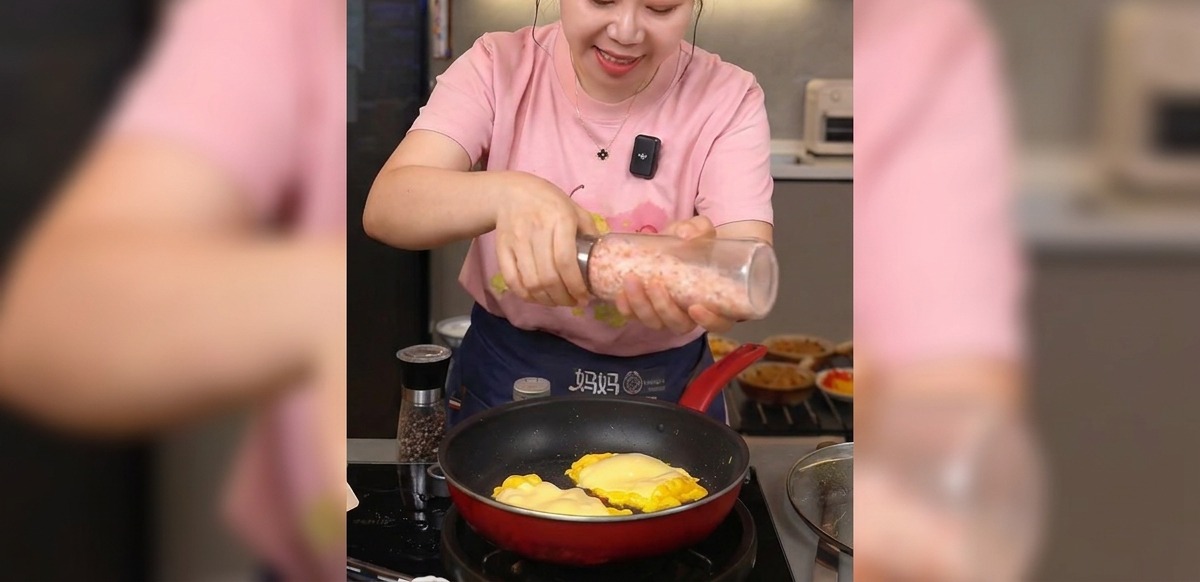 Mani che macinano sale marino rosa sopra le uova cotte e il formaggio fuso in padella.