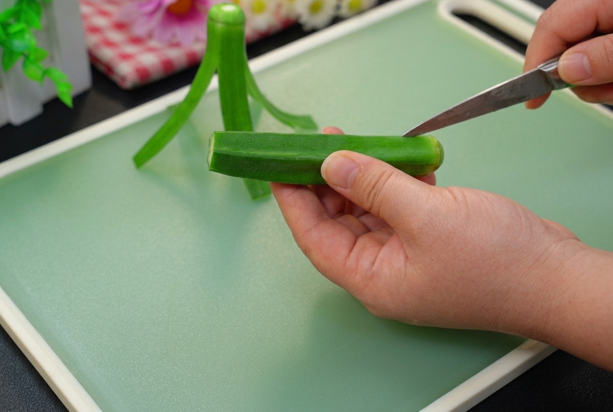 Taglio della parte superiore di unokra verde fresca con un piccolo spelucchino su un tagliere verde chiaro.