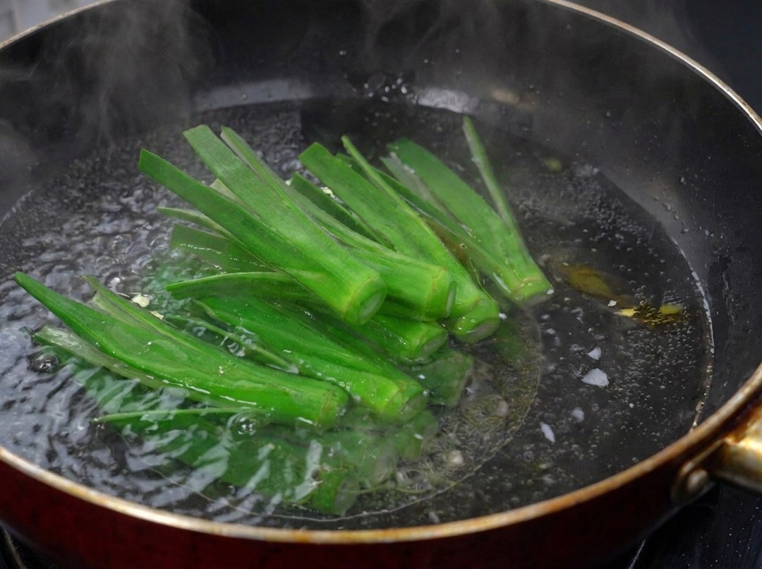Strisce di okra verde appena incise che sbollentano in un wok scuro pieno di acqua bollente.