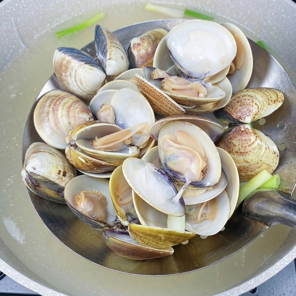 Una schiumarola di metallo con vongole calde e gusci aperti, appena prelevate dallacqua.
