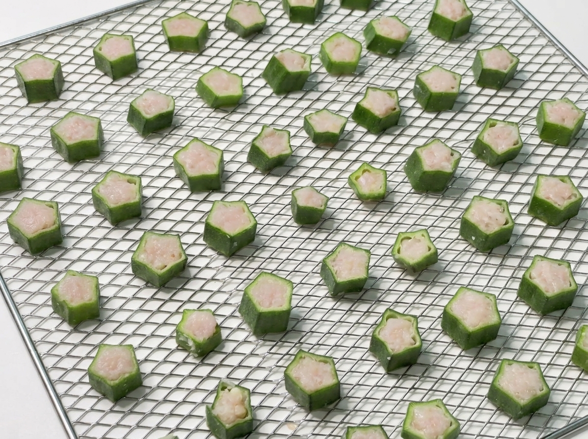 Un vassoio a rete metallica perfettamente organizzato con fette di okra farcite di pollo pronte per lessiccatore.