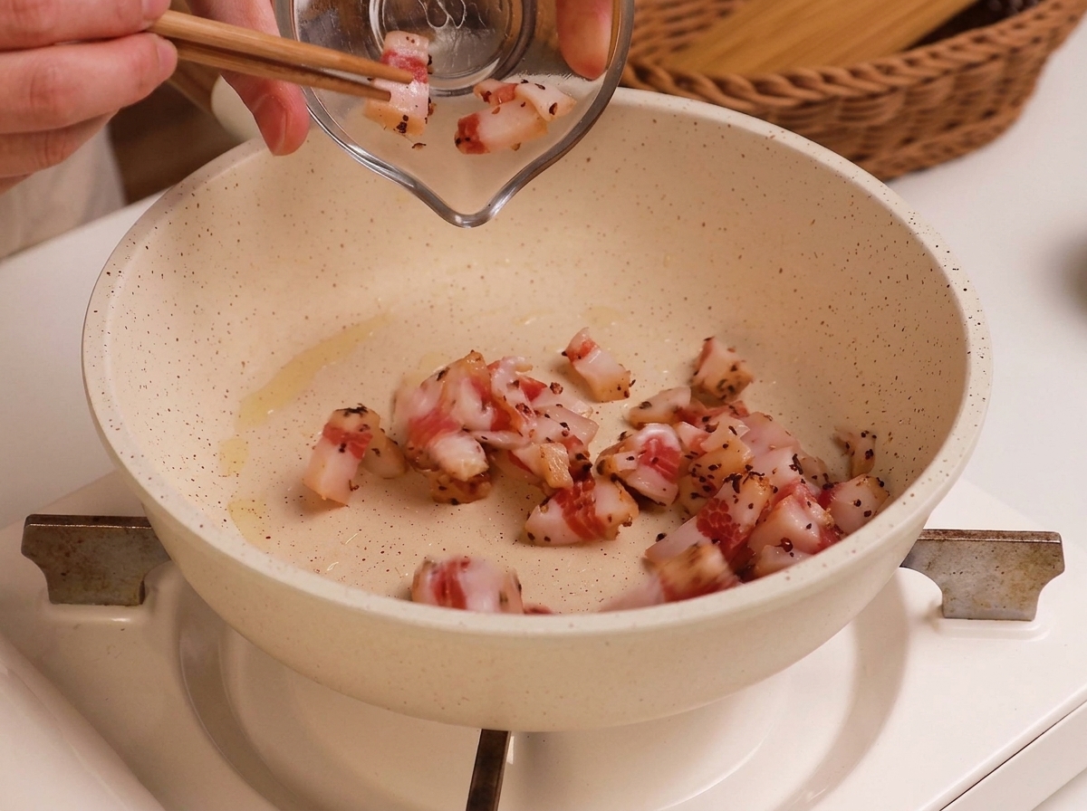 Guanciale a cubetti versato in una padella bianca con un filo dolio.