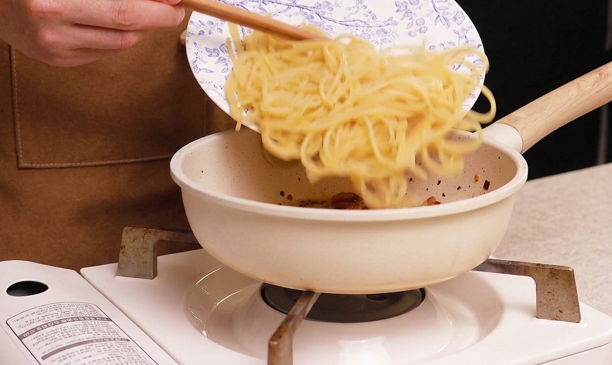 Spaghetti cotti che vengono versati nella padella con il guanciale croccante.