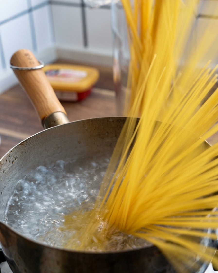 Una manciata di spaghetti secchi che vengono calati in una pentola di acqua che bolle vigorosamente.