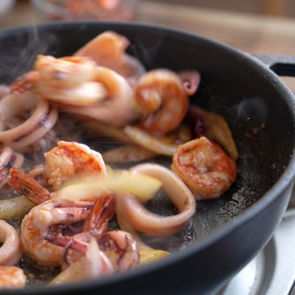 Gamberi e calamari che saltano rapidamente in padella, con i gamberi che iniziano a diventare rosa.