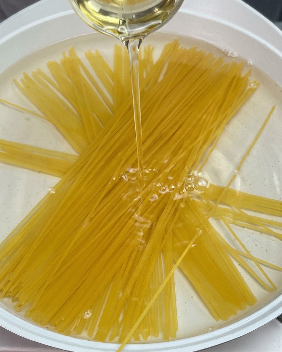 Spaghetti secchi immersi in una pentola dacqua mentre viene versato un filo dolio.