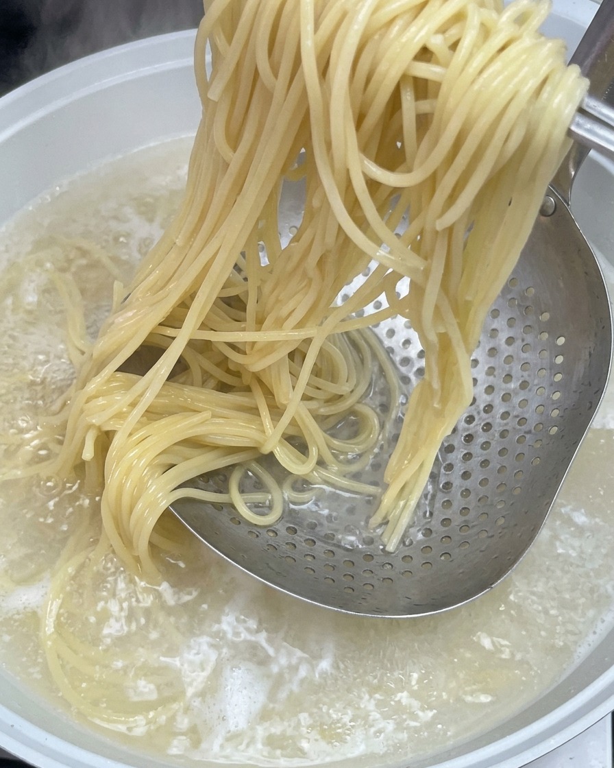 Spaghetti cotti sollevati da una pentola dacqua bollente usando una schiumarola metallica.