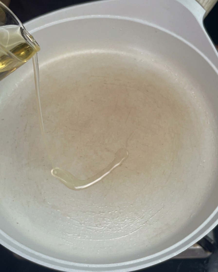 Olio di semi versato da una caraffa di vetro in una padella bianca preriscaldata.