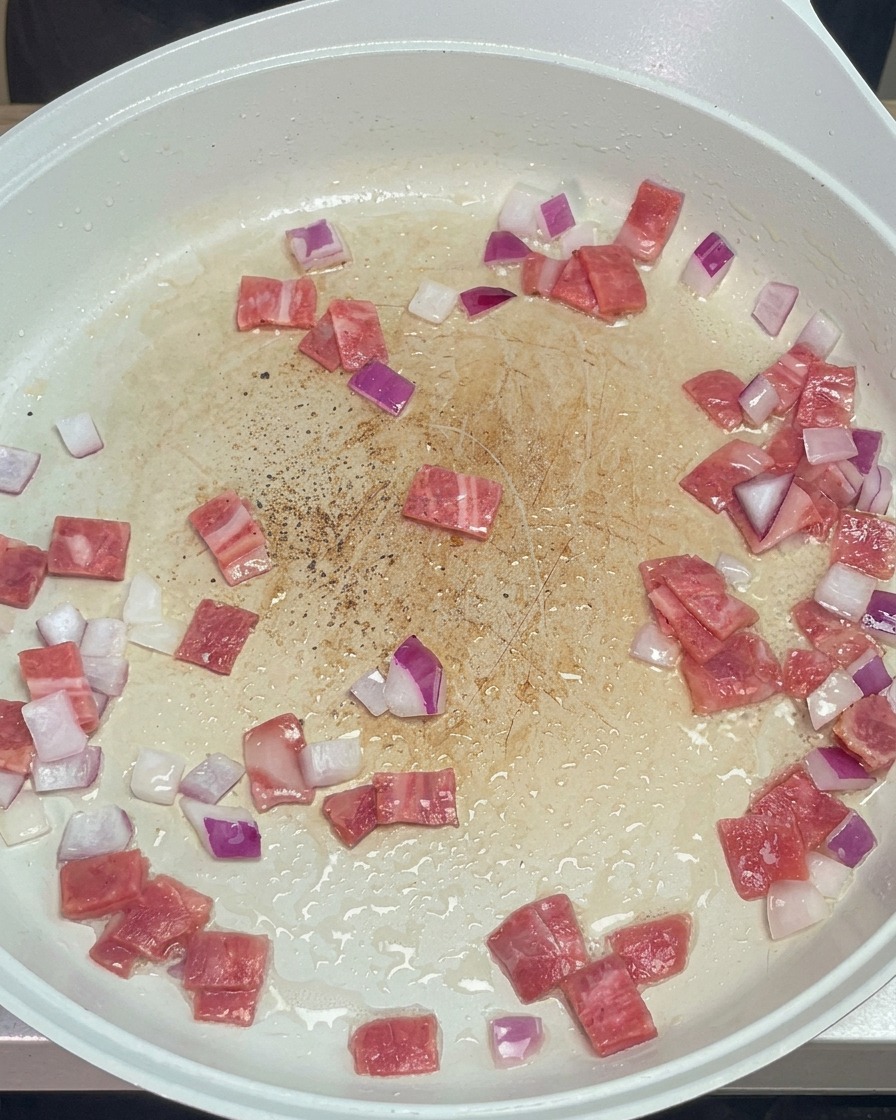 Pepe nero macinato spolverato sopra il soffritto di bacon e cipolla in padella.