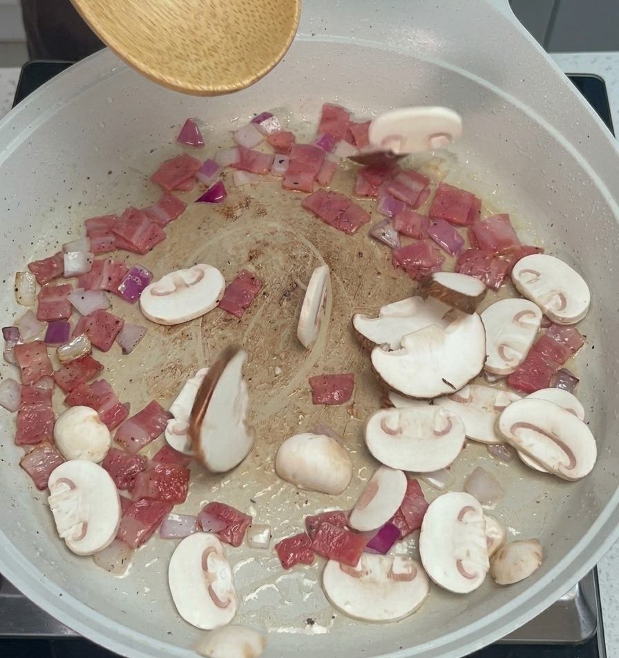 Funghi champignon e shiitake affettati aggiunti alla padella con bacon e cipolle usando un cucchiaio di legno.