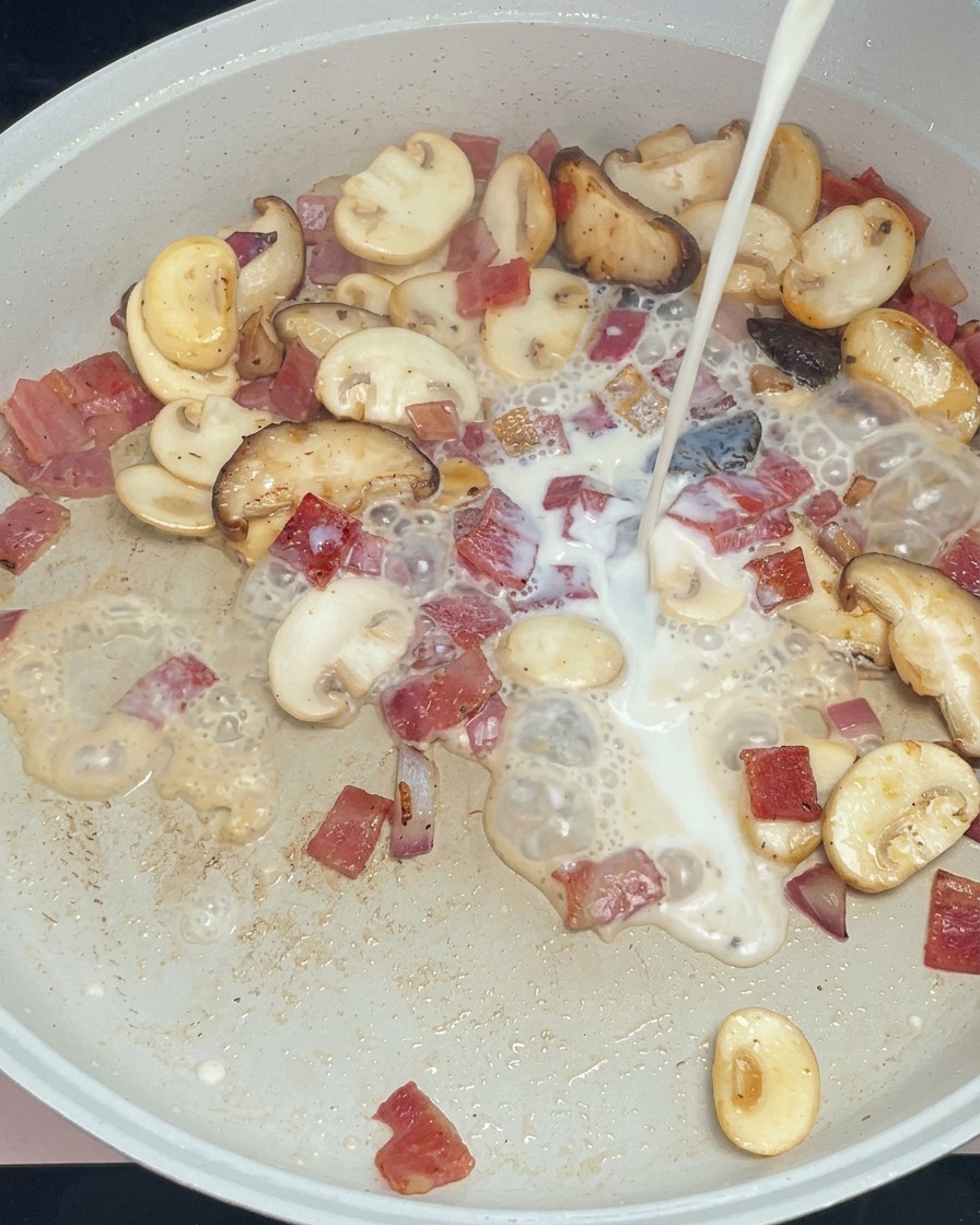 Latte bianco versato in padella con i funghi, il bacon e la cipolla rosolati.
