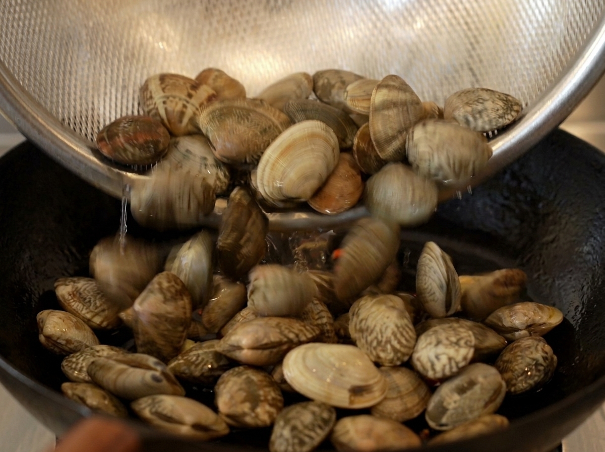 Vongole pulite versate da un colino in una padella di ghisa rovente.