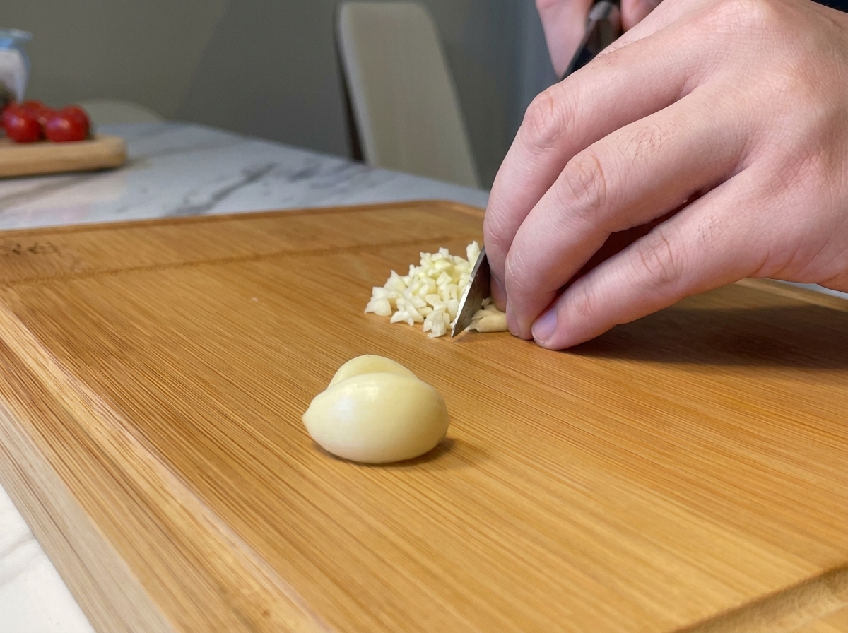 Sminuzzare finemente spicchi daglio fresco con un coltello su un tagliere di legno.