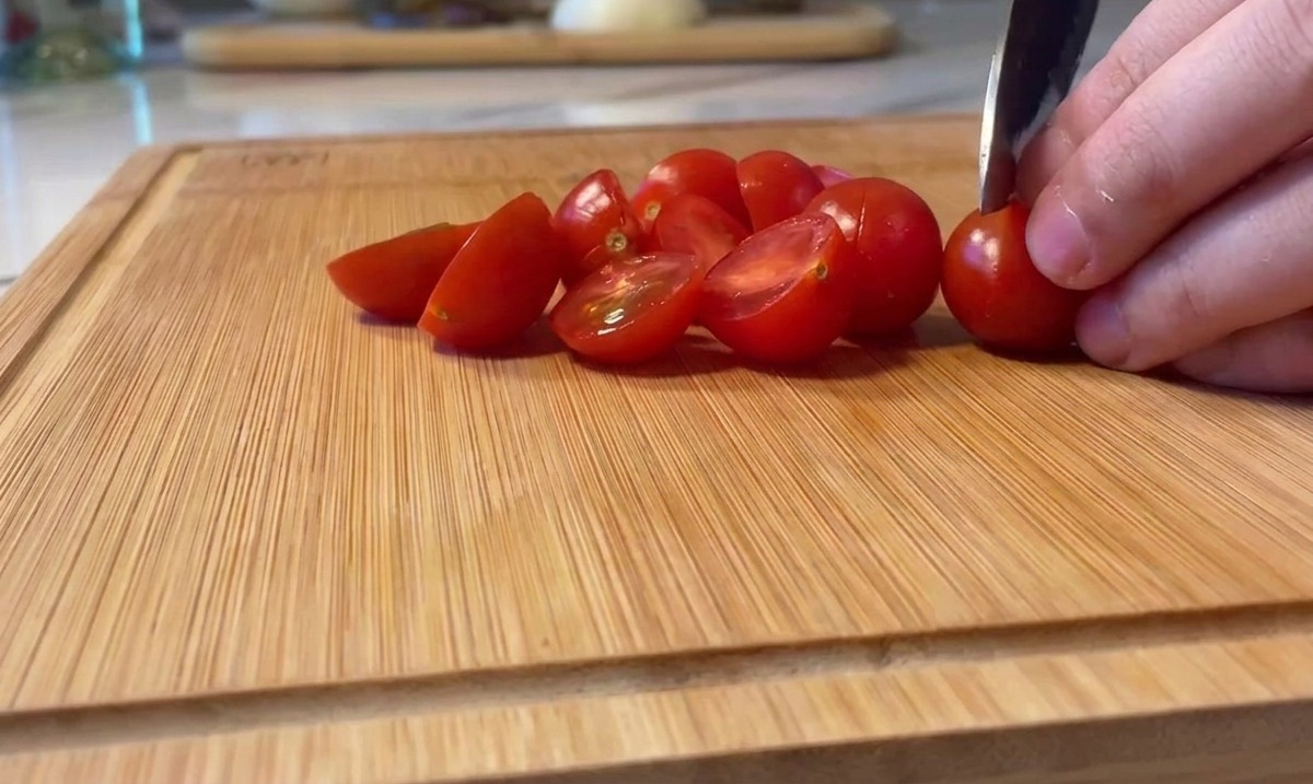 Tagliare a metà pomodorini rossi brillanti su un tagliere di legno.