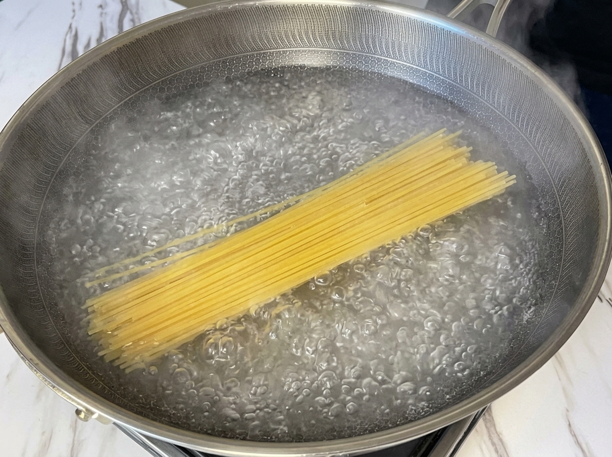 Spaghetti secchi immersi in una pentola capiente con acqua in ebollizione vivace.