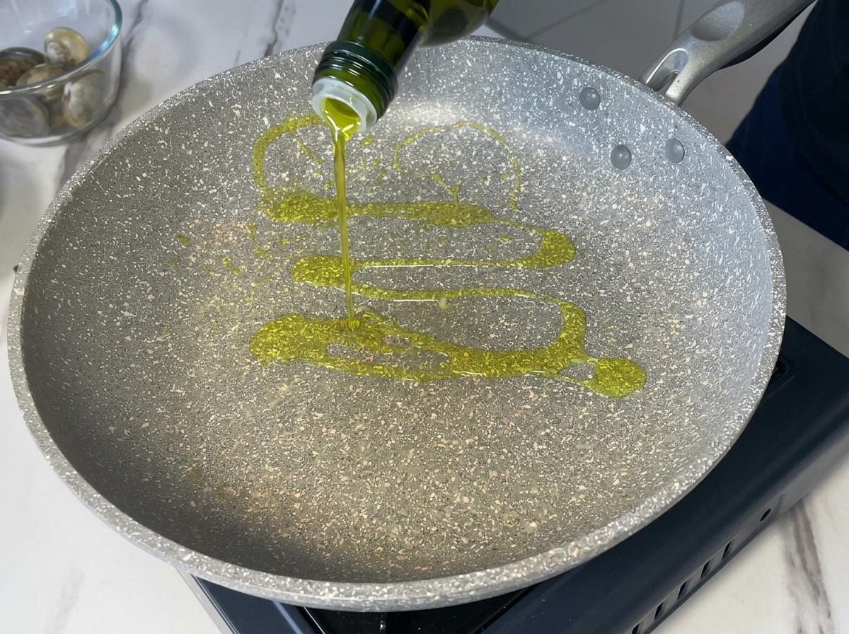 Versare olio extravergine doliva da una bottiglia scura in una padella grigia puntinata.